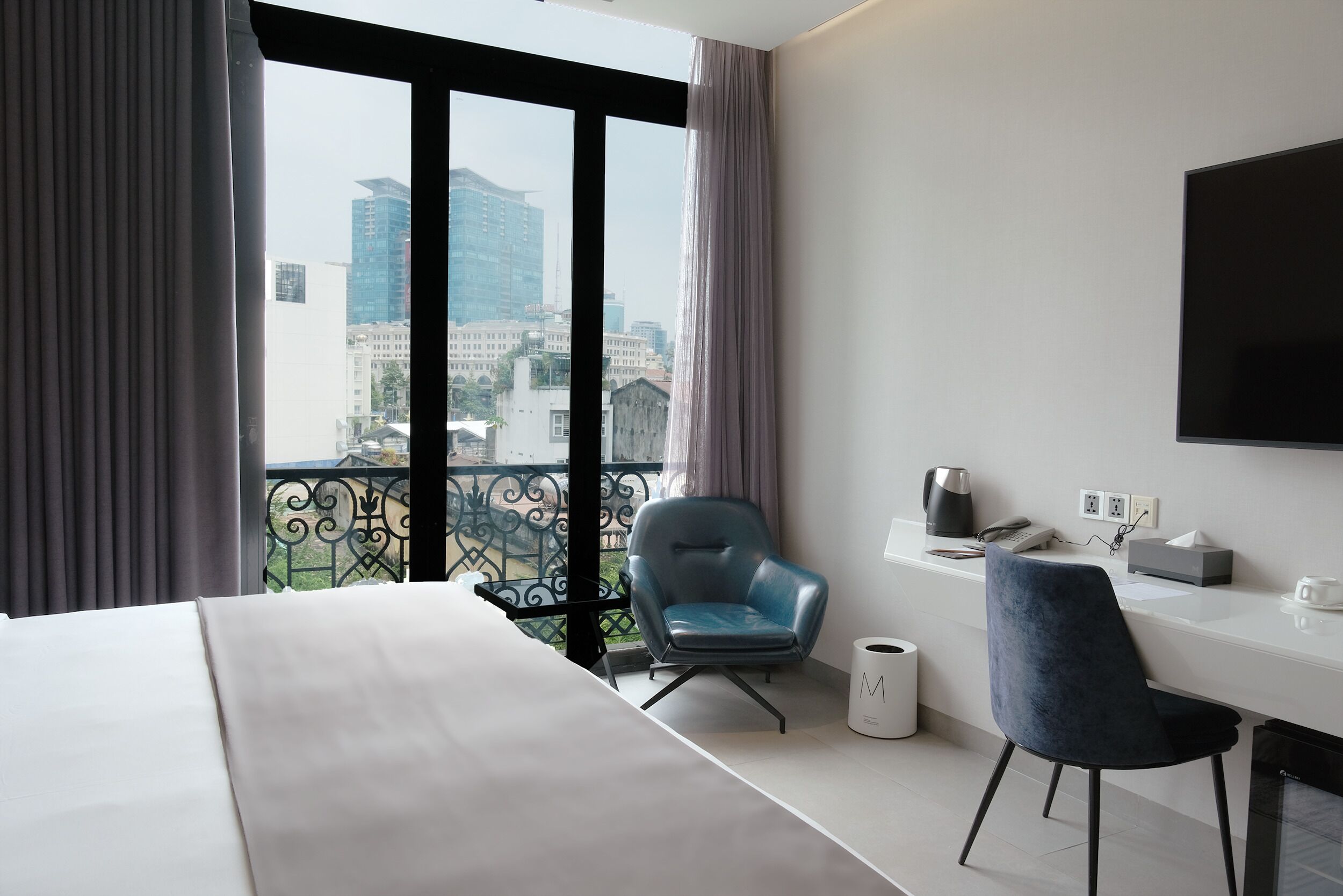 Habitación de hotel con cama, escritorio, silla, televisión y balcón con vista a la ciudad.