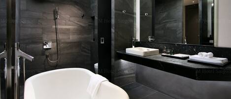 Un baño moderno con una bañera independiente, un espejo grande y una encimera negra con lavamanos y toallero.