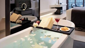 Una habitación de hotel moderna con una bañera, una zona de lectura con un libro y una bebida, y vistas a la ciudad.