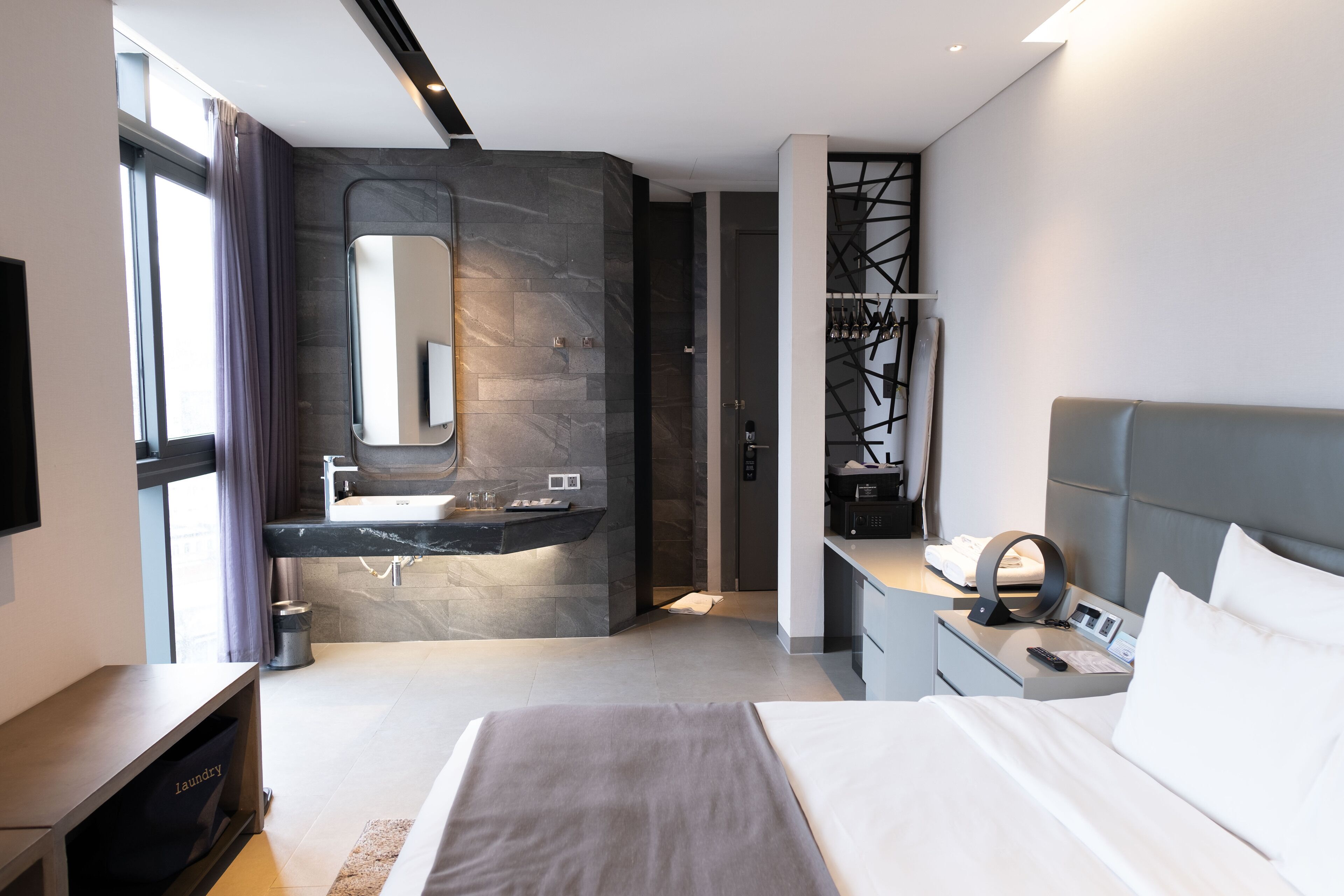 Une chambre d’hôtel moderne dotée d’un grand lit, d’une coiffeuse intégrée avec un miroir, d’un petit bureau et d’un coin salon avec un canapé.