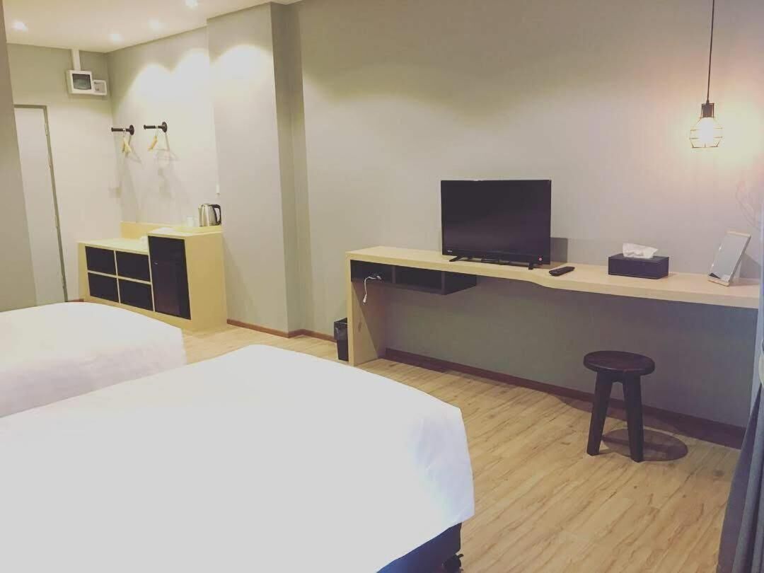 Habitación de hotel con dos camas, un televisor, un escritorio con ordenador y un taburete pequeño.
