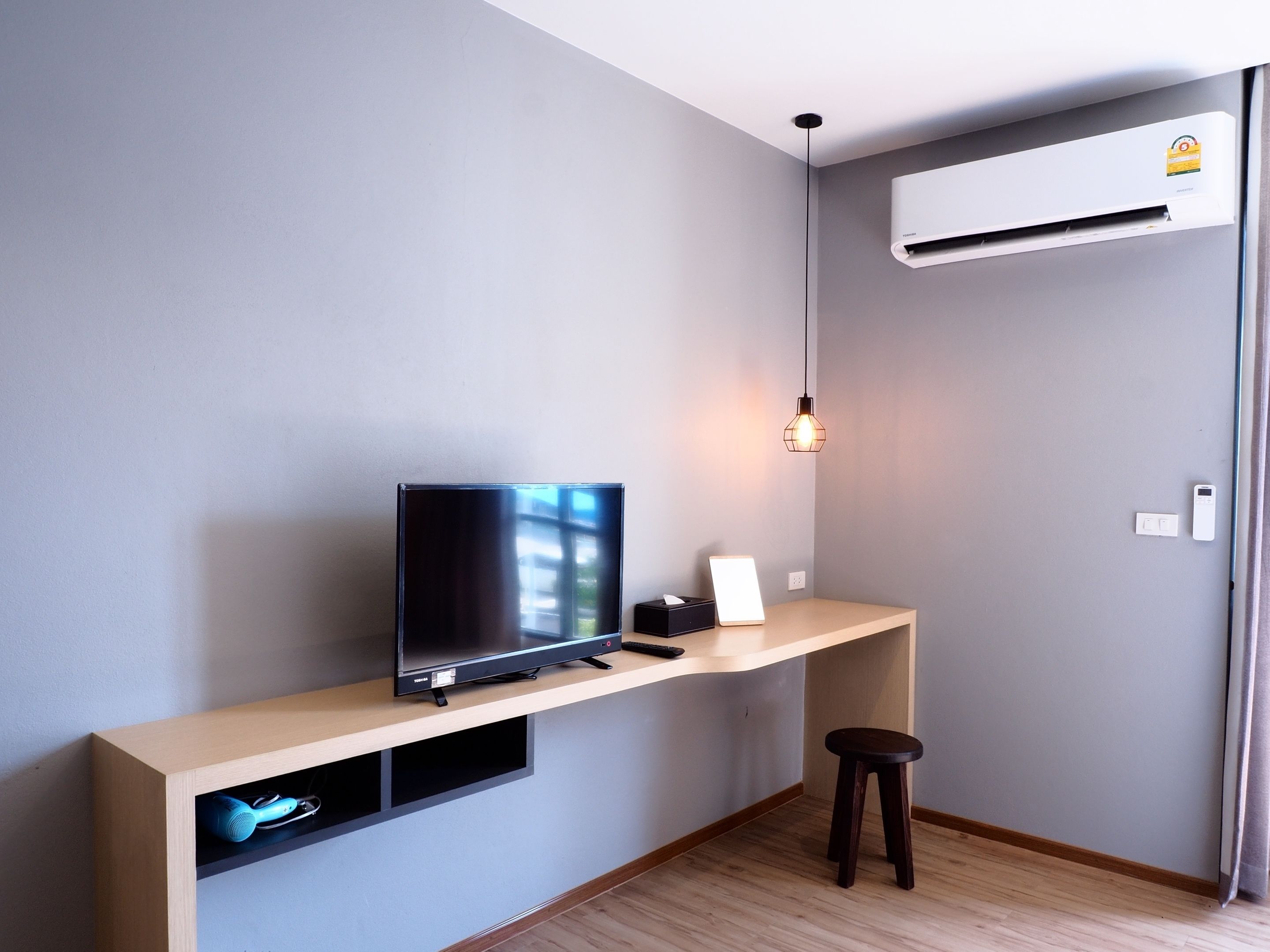 Een moderne kamer met een televisie op een houten dressoir, een klein krukje en een airconditioning.