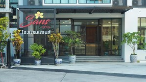 A hotel entrance with a modern facade, large windows, and potted plants at the entrance. - Sans Hotel (Ratchaburi)
