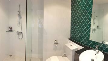 A modern bathroom with a glass-enclosed shower, a white sink, and a large mirror with a green-tiled backsplash.
