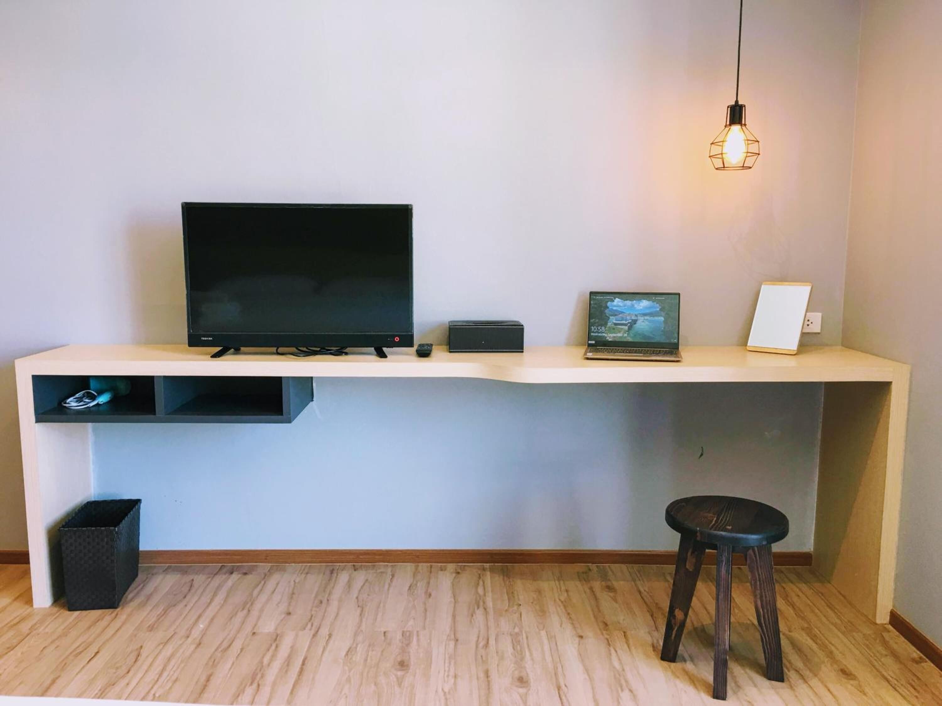 A modern workspace with a flat-screen TV, a laptop, and a desk lamp.