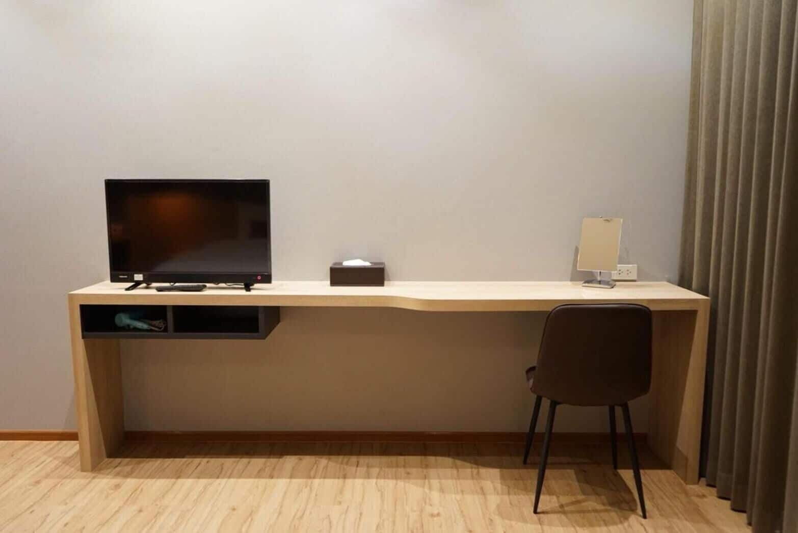 Quarto de hotel moderno com escrivaninha de madeira, televisão de tela plana, luminária e uma cadeira.