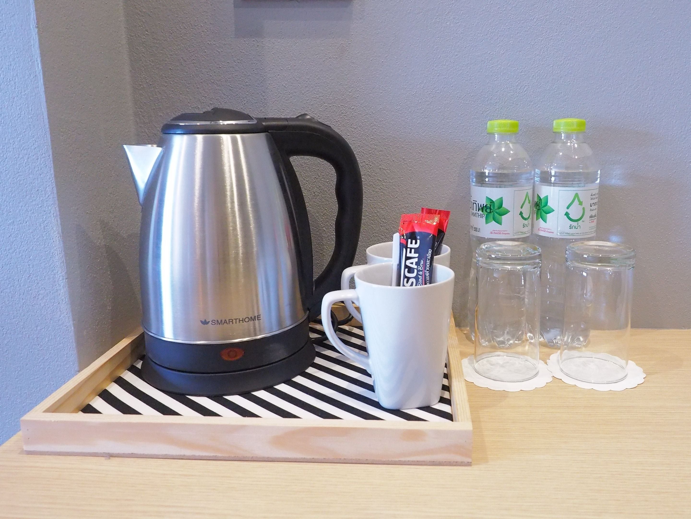 A stainless steel kettle, a white mug with a packet of snacks, and two water bottles on a tray with lids.