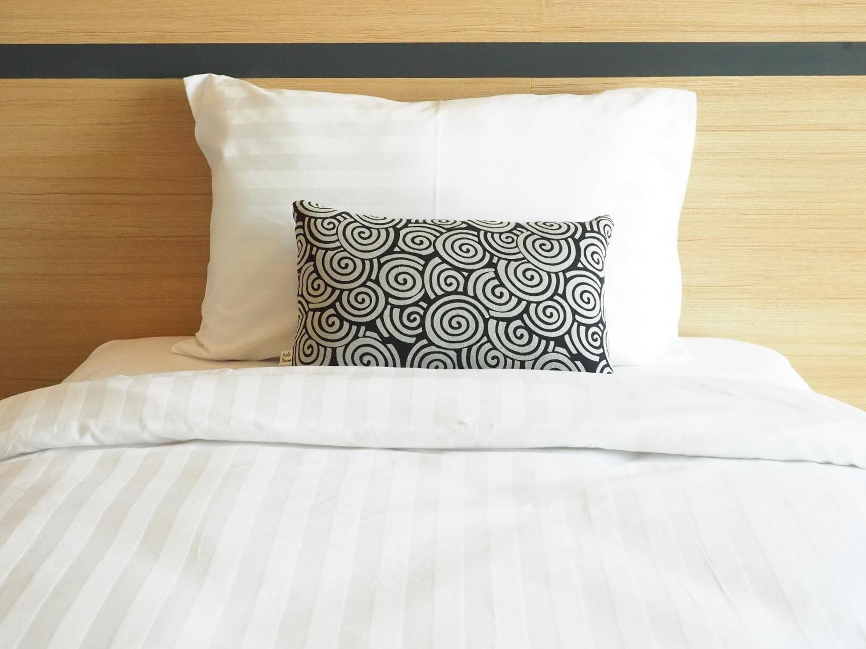 A bed with a white pillow and a black pillow with a spiral pattern.
