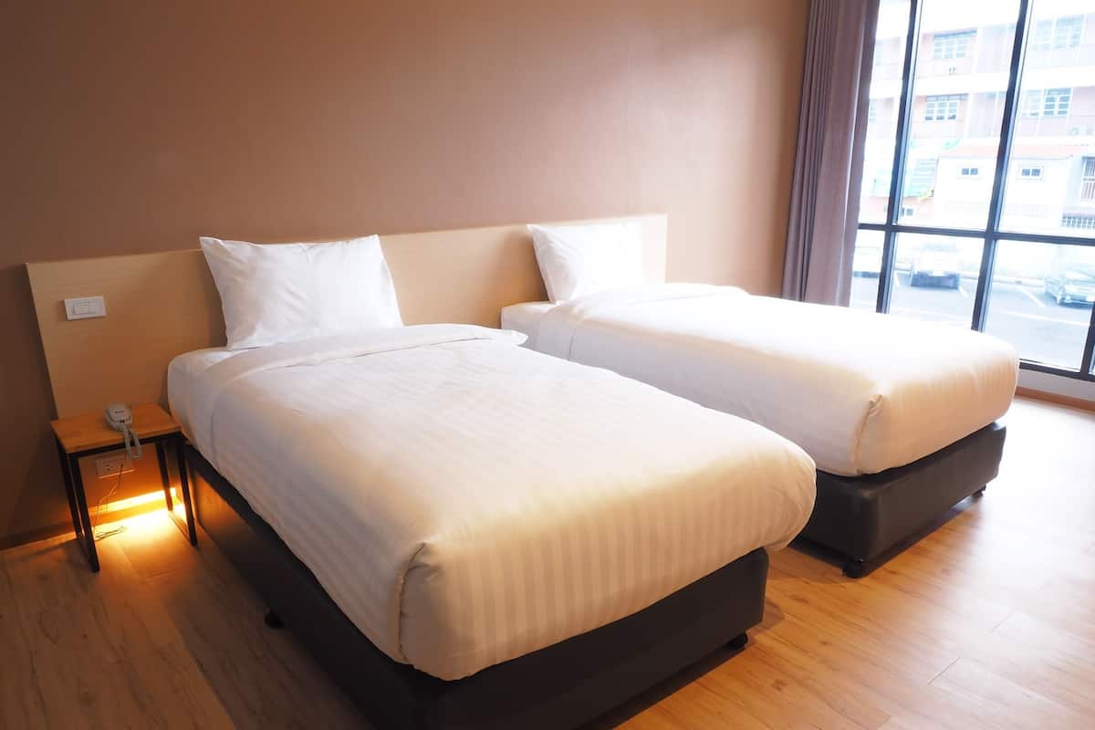 A hotel room with two beds, a bedside table with a phone, and a window with a view of buildings.