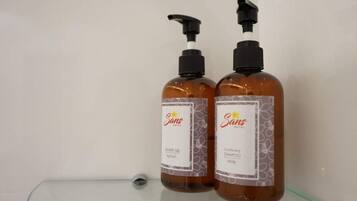 Dois frascos de gel de banho e shampoo condicionador Sans hotel sobre uma prateleira de vidro.