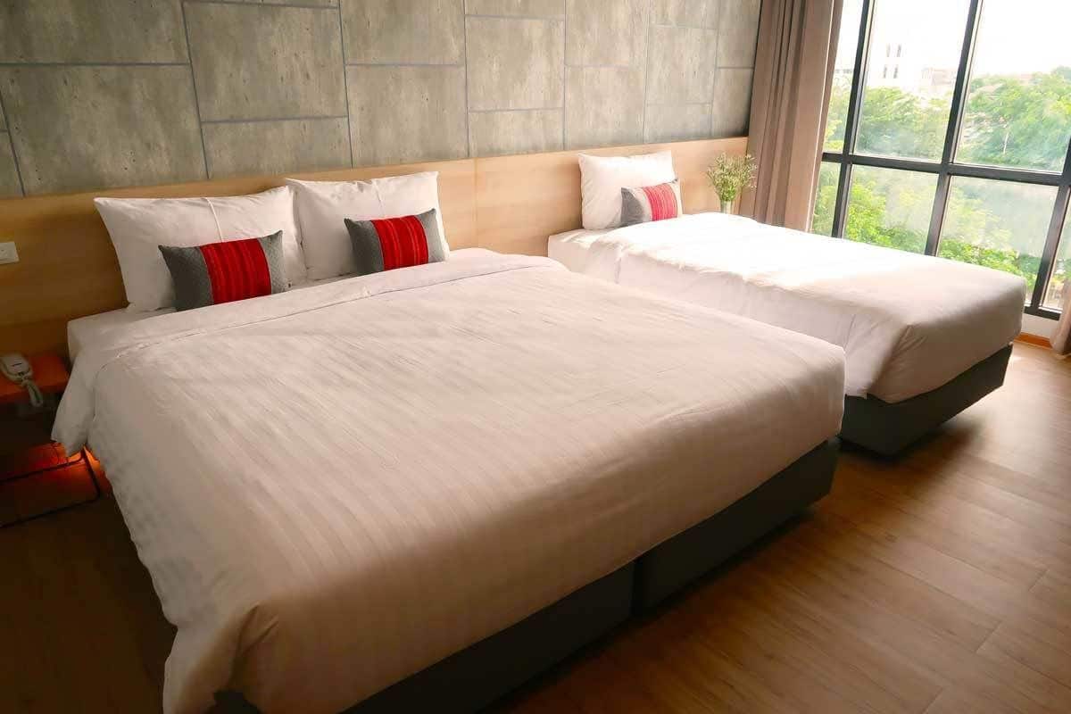 A hotel room with two beds, a wooden headboard, a large window with a view, and a telephone on the nightstand.