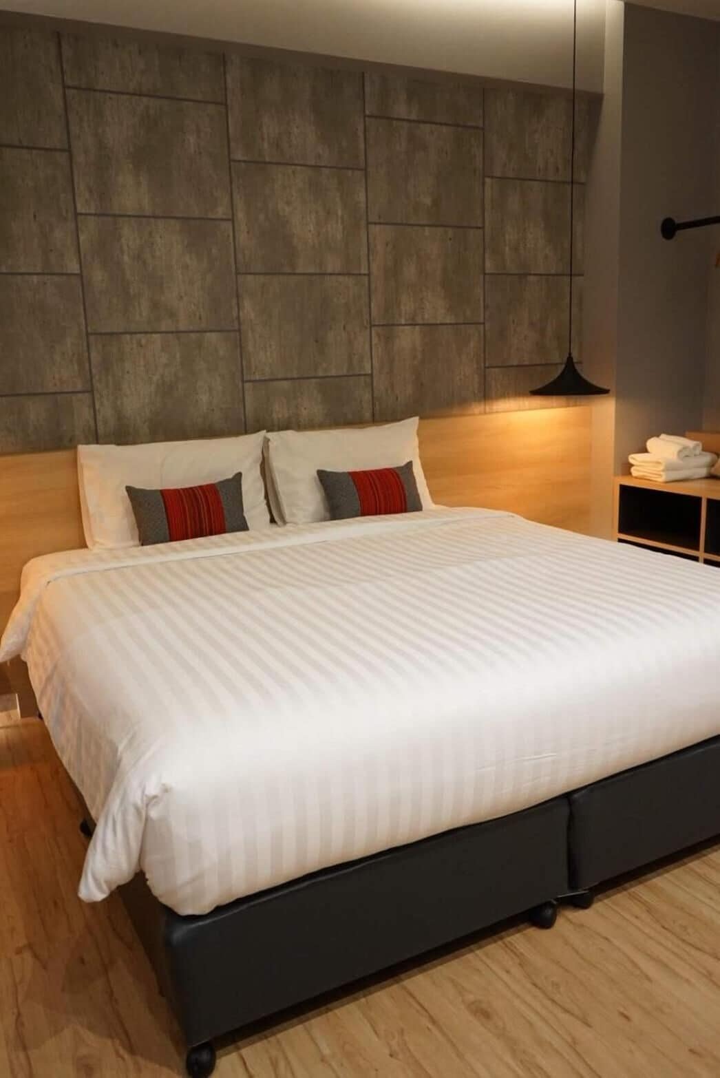 A modern bedroom with a large bed, a wooden headboard, and a nightstand with a lamp.