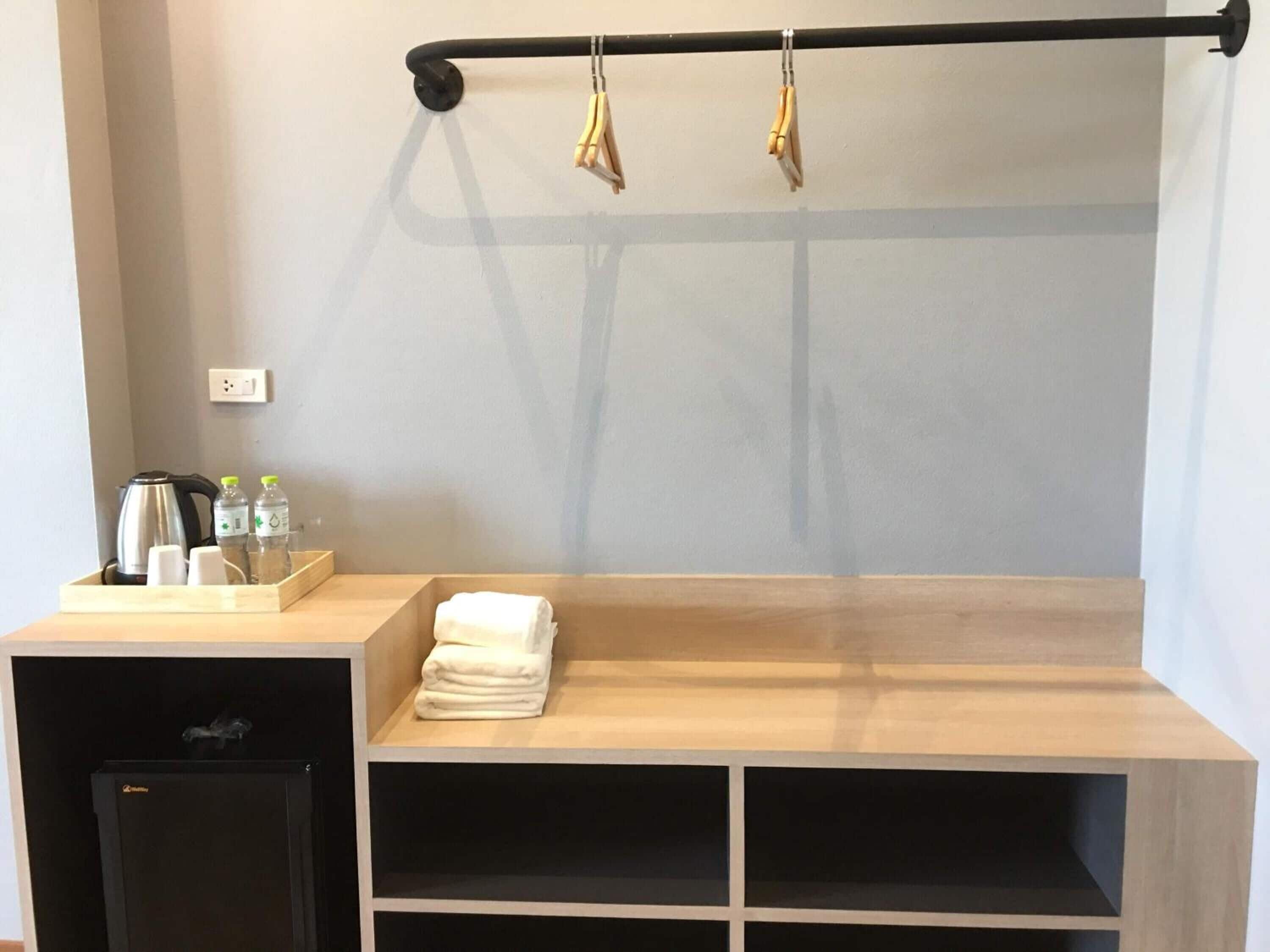 A bathroom with a wooden bench, a towel rack, a kettle, and toiletries on a tray.