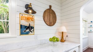 Une cuisine avec un plan de travail en marbre, une planche à découper en bois, une affiche du parc national olympique et une lampe.