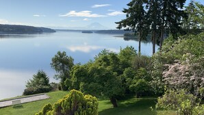 Un jardin paisible au bord d’un lac, avec un banc, une végétation luxuriante et une vue sur une montagne lointaine.