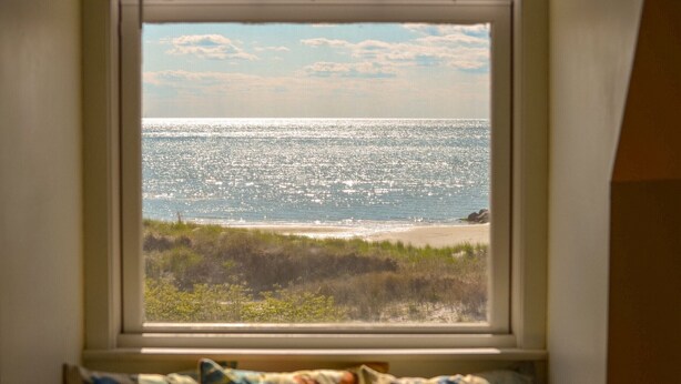 Uitzicht vanuit een raam op een strand met een zandstrand en grasduinen.