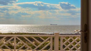 Uitzicht vanaf een balkon met een hekwerk, over een strand met een schip in de verte en een heldere lucht.