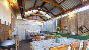 A rustic outdoor dining area with wooden furniture, a table with a patterned tablecloth, and a green railing. - A lovely rustic cottage with all the modern conveniences (Gawler South)