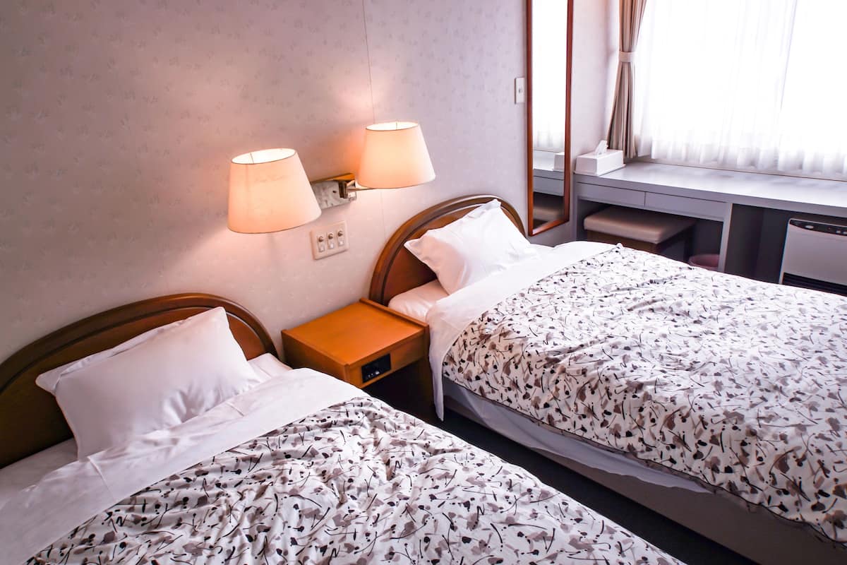 A hotel room with two single beds, a desk with a chair, a mirror, and two wall-mounted lamps.