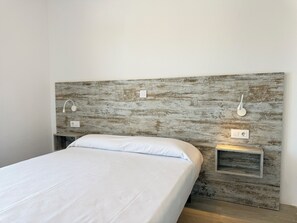 A bed with a white mattress and pillows, a wooden headboard with built-in lighting, and a small bedside table.