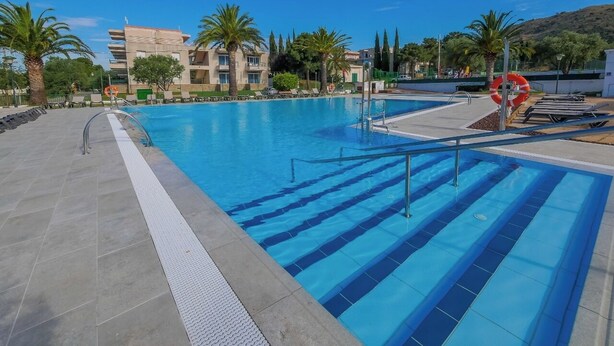 Une piscine à l’eau d’un bleu cristallin, entourée de palmiers et avec un bâtiment moderne en arrière-plan.