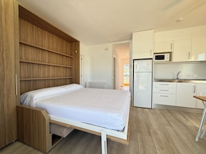 A compact room with a bed, a kitchenette, and a view of the outdoors.