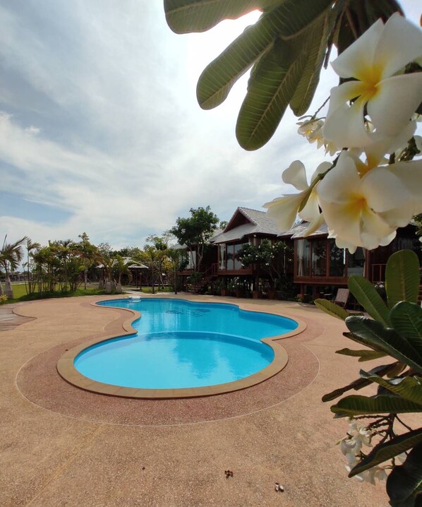 A swimming pool with a curved edge, surrounded by a pebble path and tropical plants. - Veepana Resort (Ban Laem)