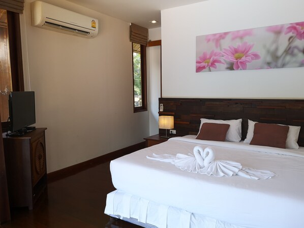 Habitación de hotel con una cama grande, un televisor de pantalla plana sobre un mueble de madera, aire acondicionado, una lámpara de noche y un cuadro con motivos florales en la pared.