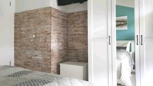 Ein Schlafzimmer mit einer ziegelmusterigen Wand, einem weißen Kleiderschrank und einem Bett mit einem gemusterten Überwurf.