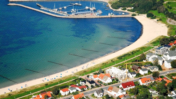 Eine Luftaufnahme einer Küstenregion mit einem Yachthafen, Strand und Wohngebäuden.
