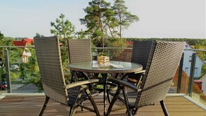 Ein runder Glastisch mit Korbstühlen auf einer Holzterrasse.
