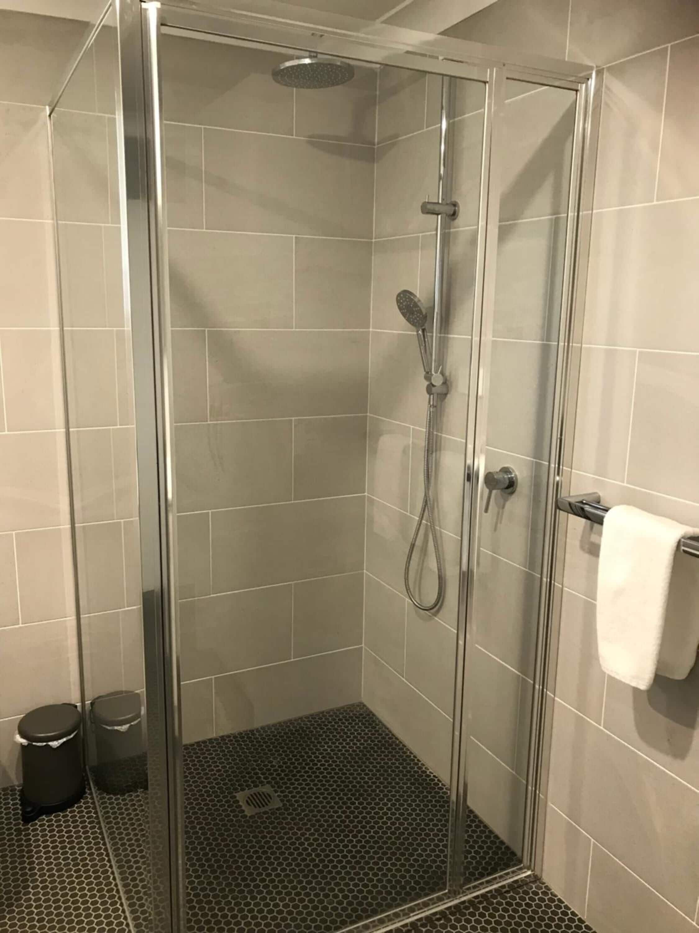 A glass-enclosed shower with a handheld showerhead and a wall-mounted faucet.