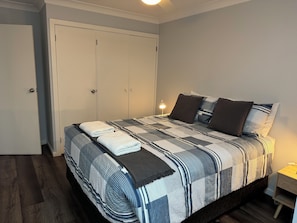 A neatly made bed with a striped bedspread and pillows, a bedside lamp, and a wardrobe with a door. - Ulladulla Motel (Ulladulla)