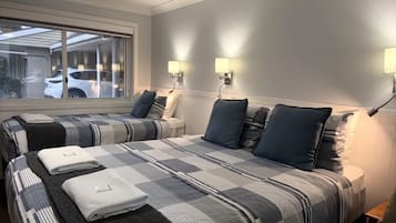 A hotel room with two beds, a window with a view of a parked car, and wall-mounted lamps.