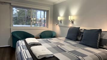 A hotel room with a bed, two chairs, a window, and wall-mounted lights.