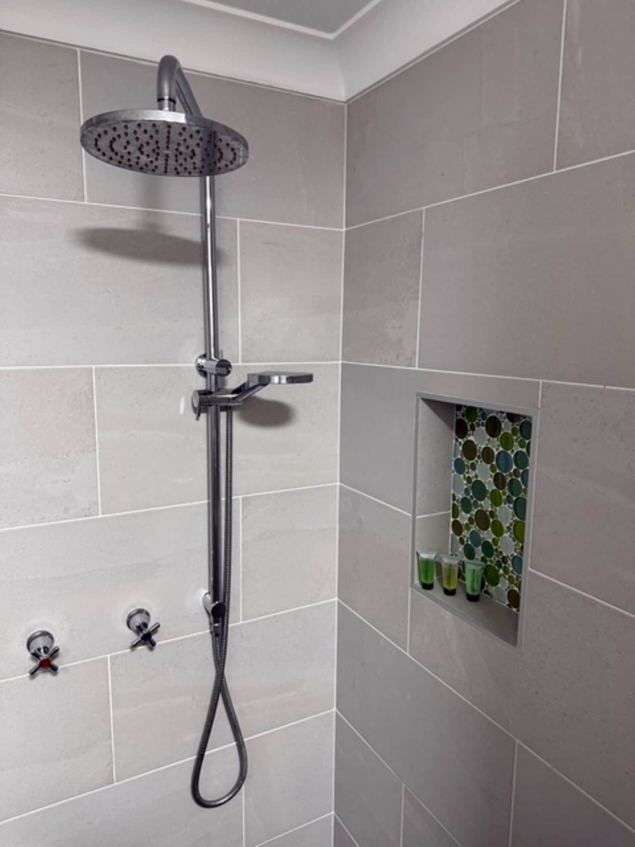 Eine Dusche mit Duschbrause, Armaturen an der Wand und einer kleinen Ablage für Pflegeprodukte.