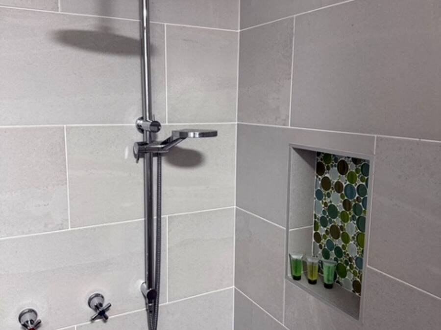 Eine Dusche mit Duschbrause, Armaturen an der Wand und einer kleinen Ablage für Pflegeprodukte.