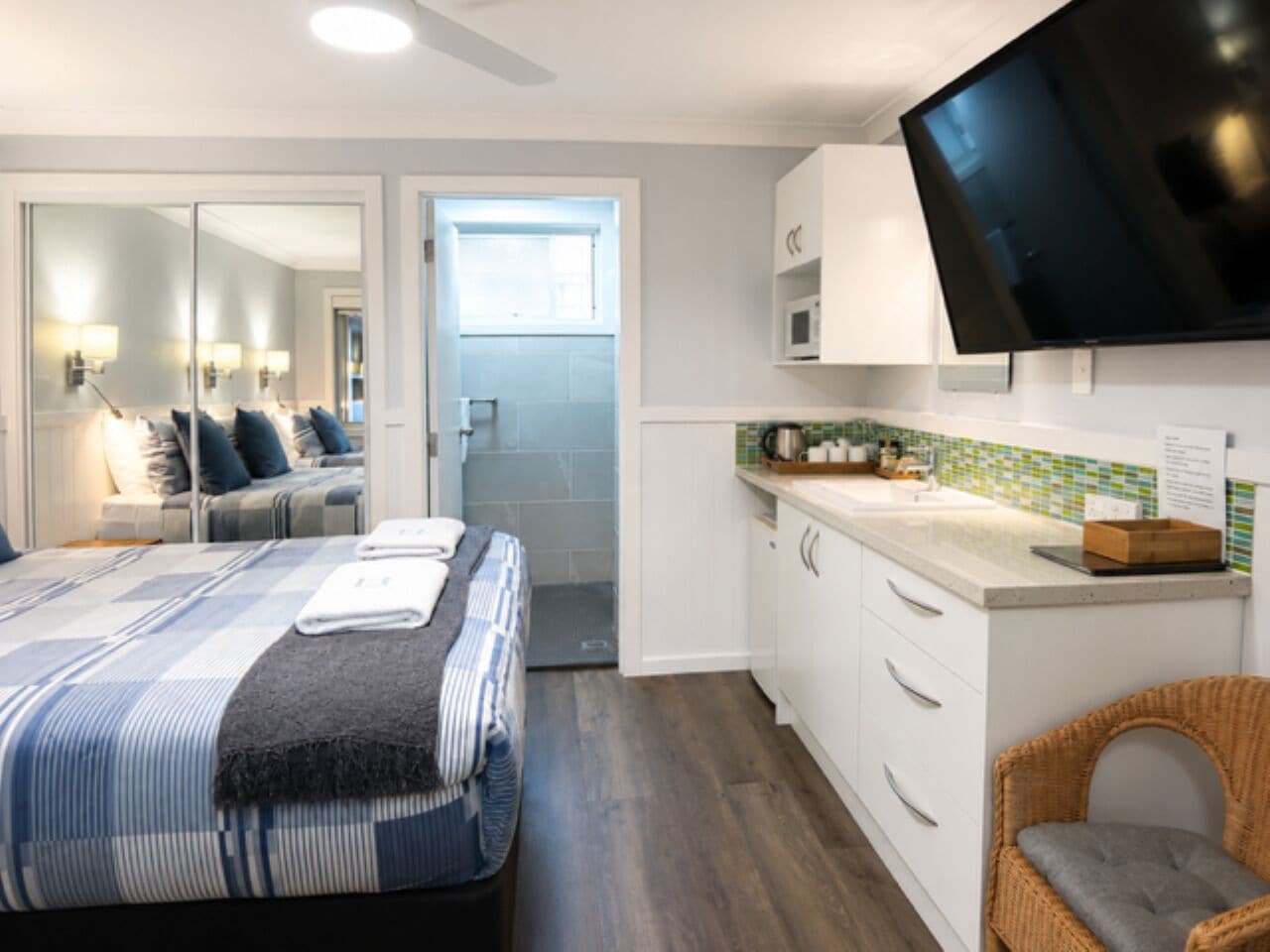 A hotel room with a bed, a television, a kitchenette, and a bathroom.