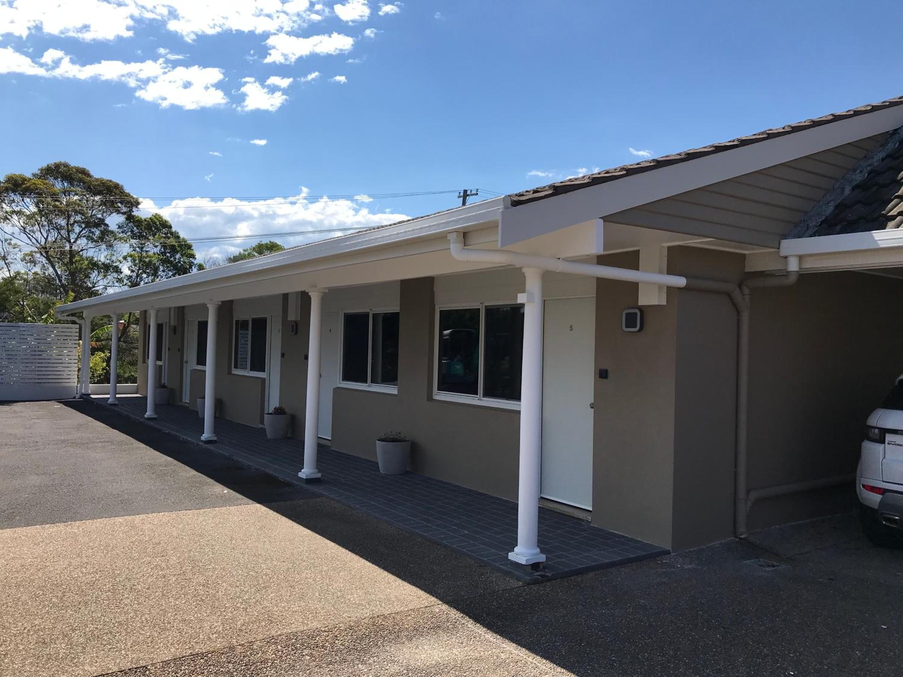 Un motel doté d’un espace extérieur abrité avec des sièges, d’un parking et d’un bâtiment à la façade beige.