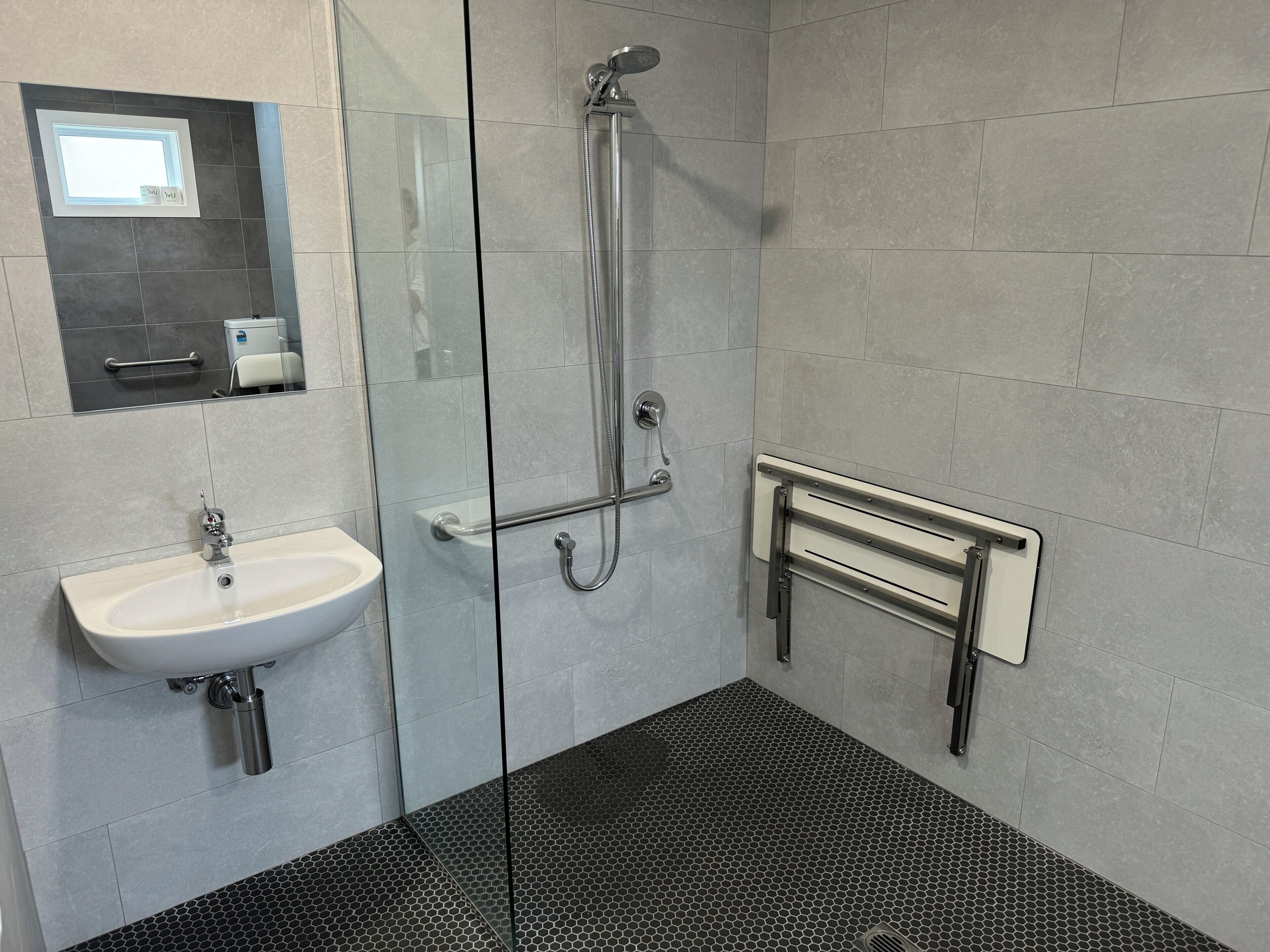 A modern bathroom with a glass shower enclosure, a white sink, and a handrail.