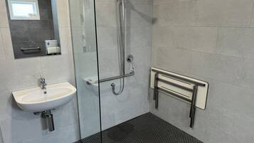 A modern bathroom with a glass shower enclosure, a white sink, and a handrail.