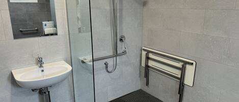 Un baño moderno con cabina de ducha de vidrio, lavabo blanco y barandilla.