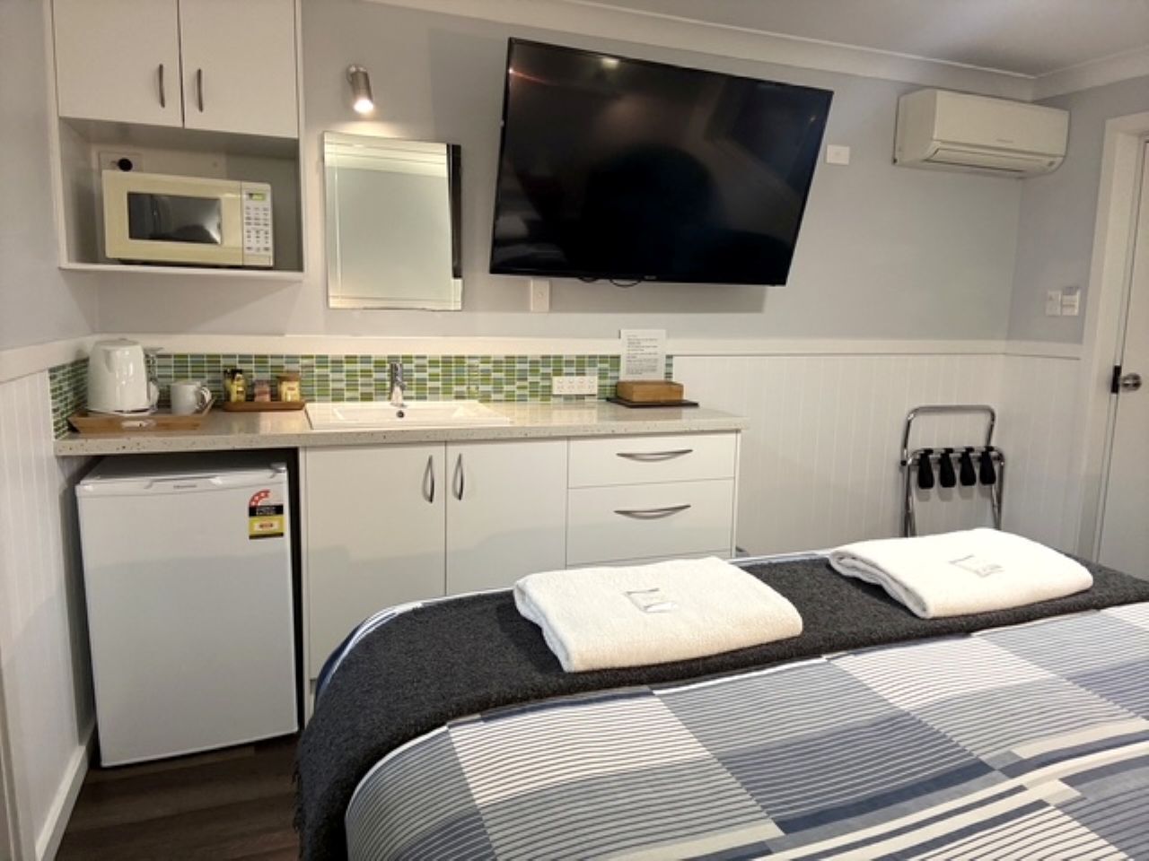 Habitación de hotel con cama, kitchenette, televisión de pantalla plana y perchero.