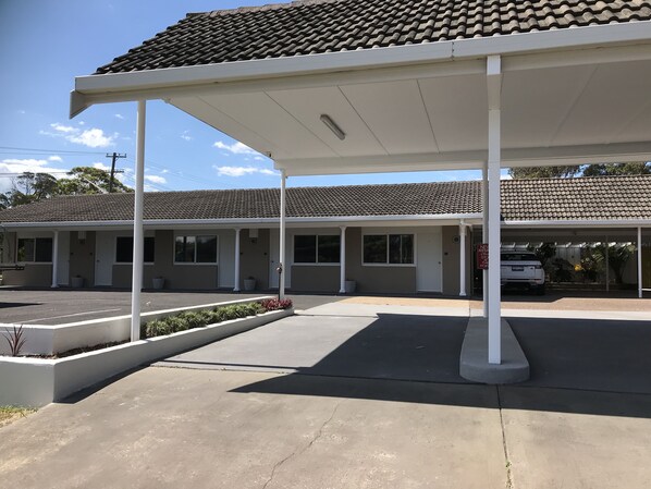 A motel with a covered parking area, a row of rooms, and a sign indicating new arrivals.