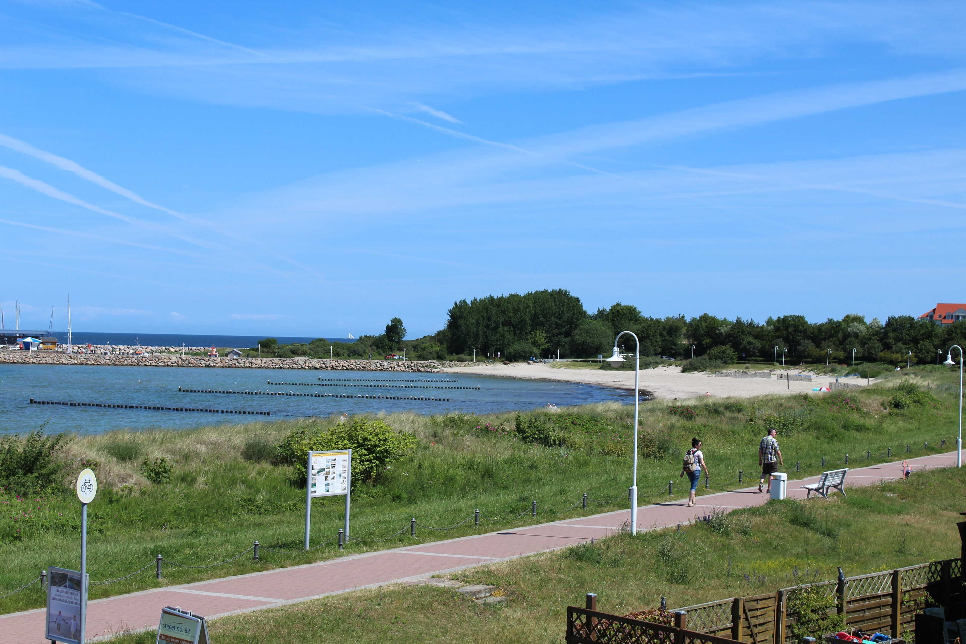 A riverside walkway with a bench, a sign, and a path leading to a beach.