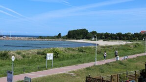 Un passeig al costat del riu amb una banca, un senyal i un camí cap a una platja.