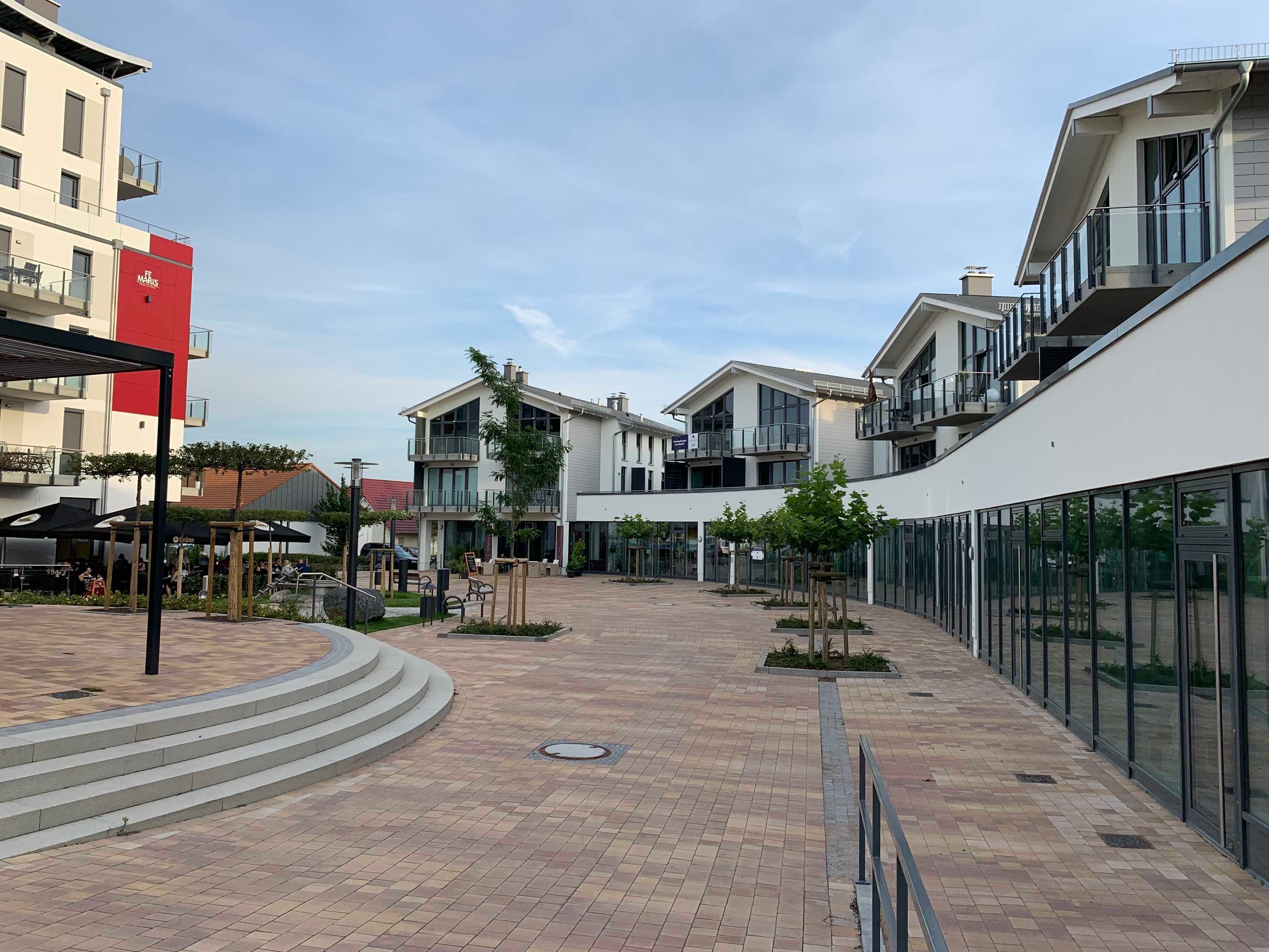 A modern outdoor area with a paved walkway, seating areas, and a small garden with trees.