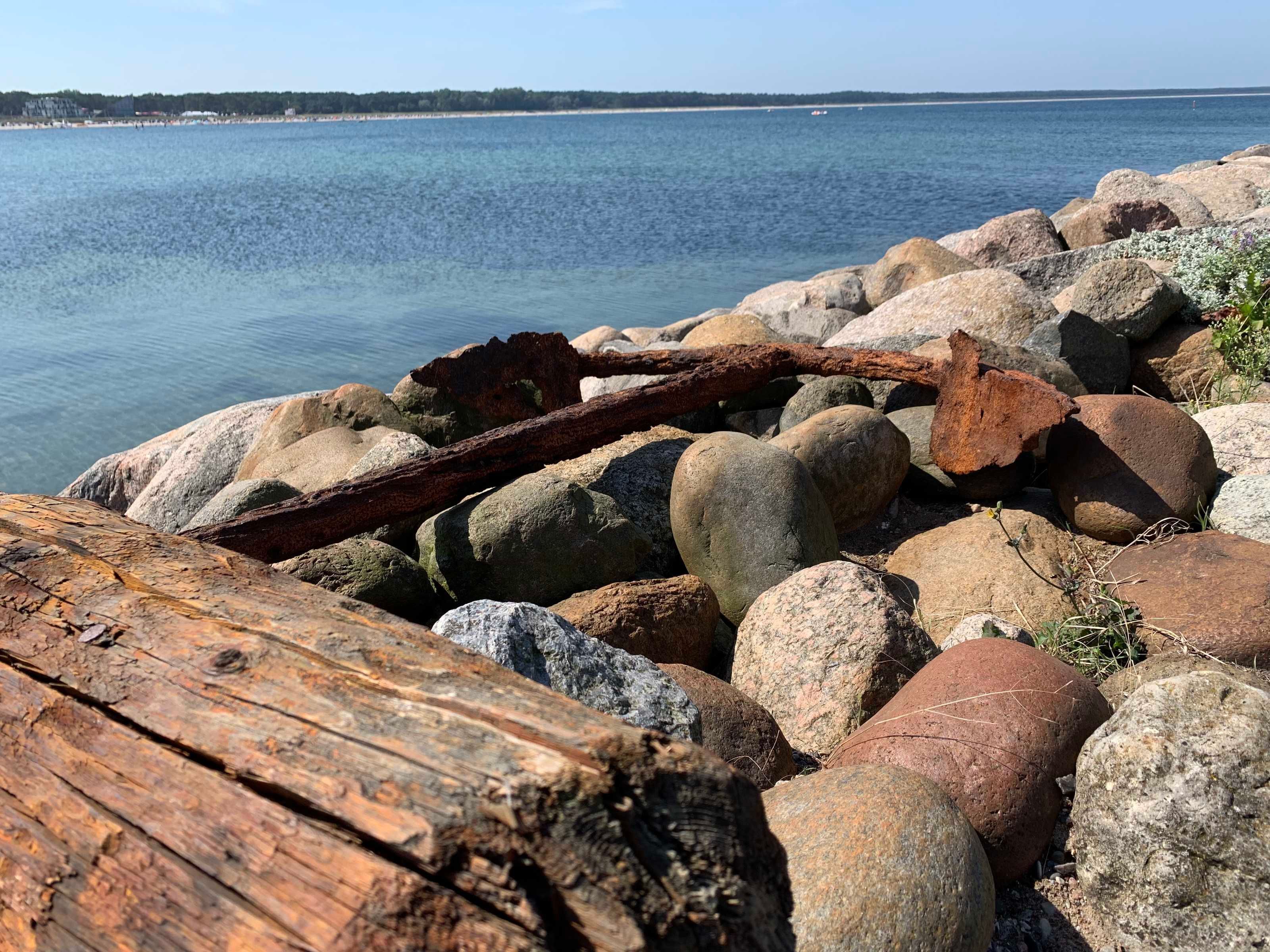 A rocky shoreline with a large rusted metal object and a wooden log.