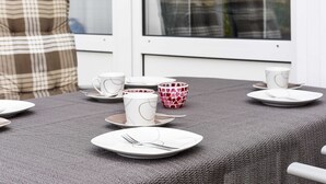 A dining table set with plates, cups, and a bowl, with a window and a plaid cushion in the background. - Vacation cottage Brigitte, Germany (Esens)