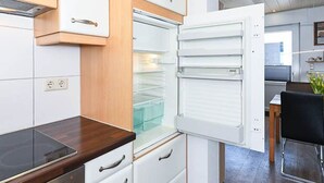 A modern kitchen with white cabinets, a built-in oven, and a dining area with a table and chairs. - Vacation cottage Brigitte, Germany (Esens)